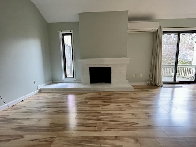 unfurnished living room with a wall mounted air conditioner, light hardwood / wood-style floors, vaulted ceiling, and a brick fireplace