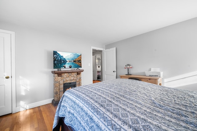 bedroom featuring hardwood / wood-style floors and a stone fireplace