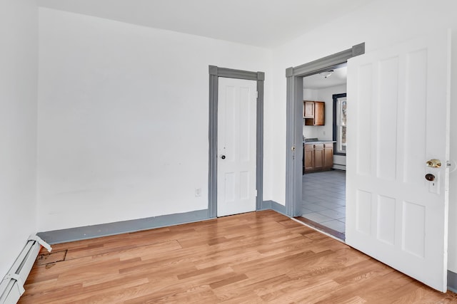 unfurnished room with baseboard heating and light hardwood / wood-style flooring