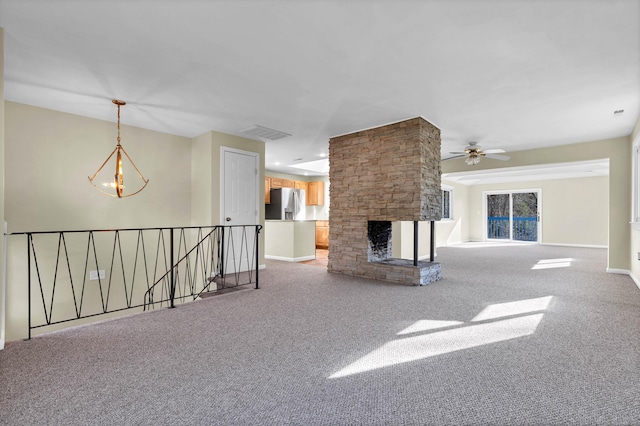 unfurnished living room with ceiling fan with notable chandelier, a fireplace, and light carpet