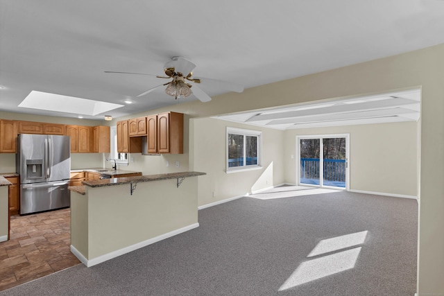 kitchen with kitchen peninsula, stainless steel refrigerator with ice dispenser, light carpet, a skylight, and a breakfast bar area