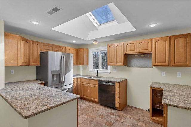 kitchen featuring a skylight, light stone countertops, dishwasher, sink, and stainless steel fridge