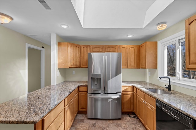 kitchen with stainless steel fridge, a skylight, light stone counters, sink, and black dishwasher