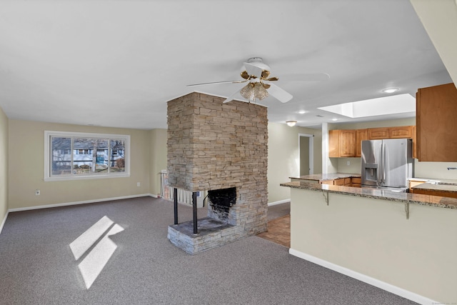 unfurnished living room with a fireplace, a skylight, dark carpet, and ceiling fan