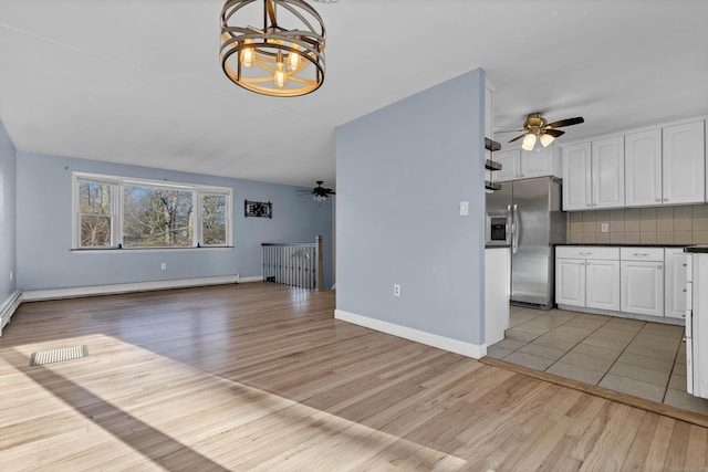 unfurnished living room featuring ceiling fan with notable chandelier, light hardwood / wood-style floors, and a baseboard radiator