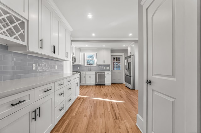 kitchen with decorative backsplash, white cabinetry, stainless steel appliances, and light wood-type flooring