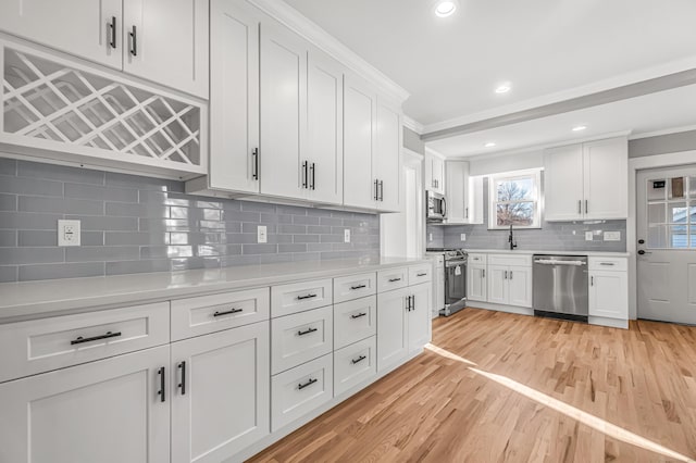 kitchen featuring white cabinets, light wood-type flooring, ornamental molding, and stainless steel appliances