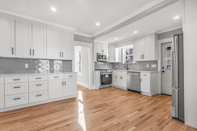 kitchen with white cabinets, light hardwood / wood-style floors, appliances with stainless steel finishes, and tasteful backsplash