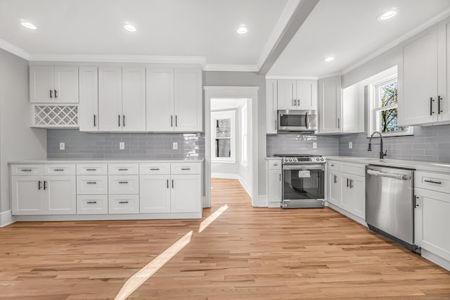 kitchen featuring stainless steel appliances, crown molding, sink, light hardwood / wood-style flooring, and white cabinetry