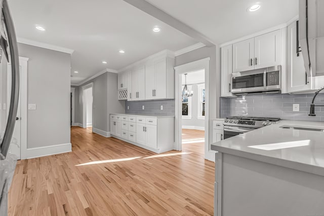 kitchen with sink, light wood-type flooring, ornamental molding, white cabinetry, and stainless steel appliances