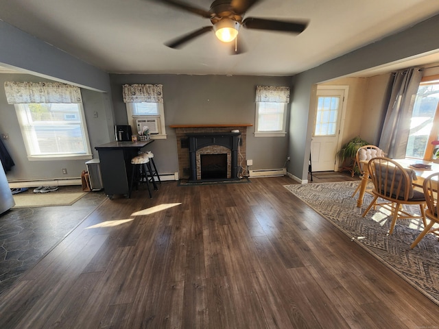 living room featuring a baseboard heating unit, a healthy amount of sunlight, dark hardwood / wood-style floors, and a brick fireplace