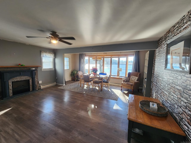 living room featuring ceiling fan, dark wood-type flooring, a stone fireplace, a baseboard heating unit, and a water view