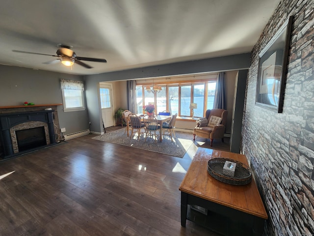 living room featuring dark hardwood / wood-style flooring, ceiling fan, a baseboard heating unit, a water view, and a fireplace