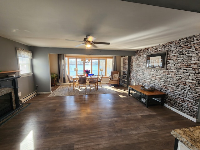 unfurnished dining area featuring dark hardwood / wood-style floors, ceiling fan, a stone fireplace, and a baseboard heating unit