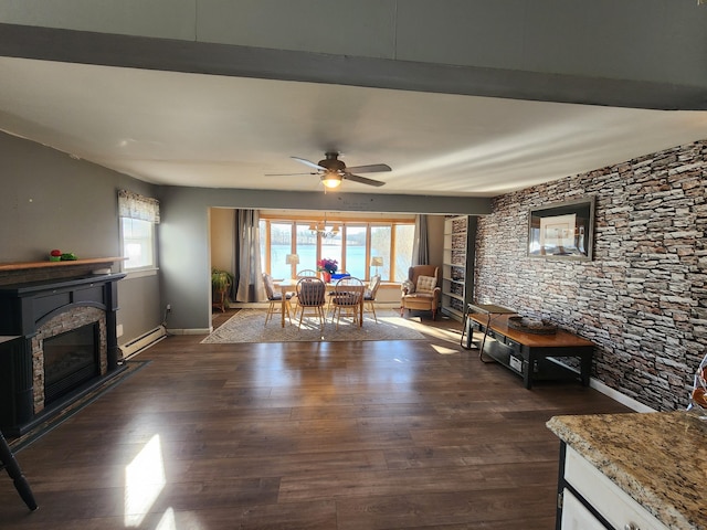 unfurnished living room featuring dark hardwood / wood-style flooring, a stone fireplace, ceiling fan, and a baseboard heating unit