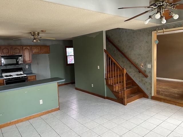 kitchen featuring ceiling fan, light tile patterned flooring, a textured ceiling, and gas range gas stove