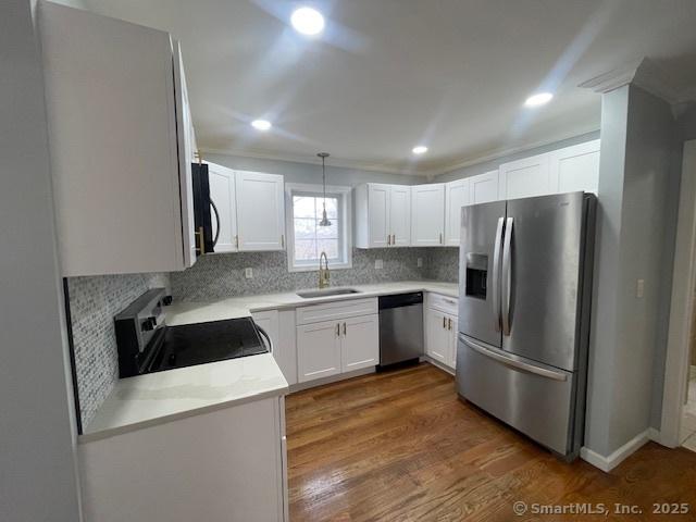 kitchen with appliances with stainless steel finishes, sink, pendant lighting, dark hardwood / wood-style floors, and white cabinetry