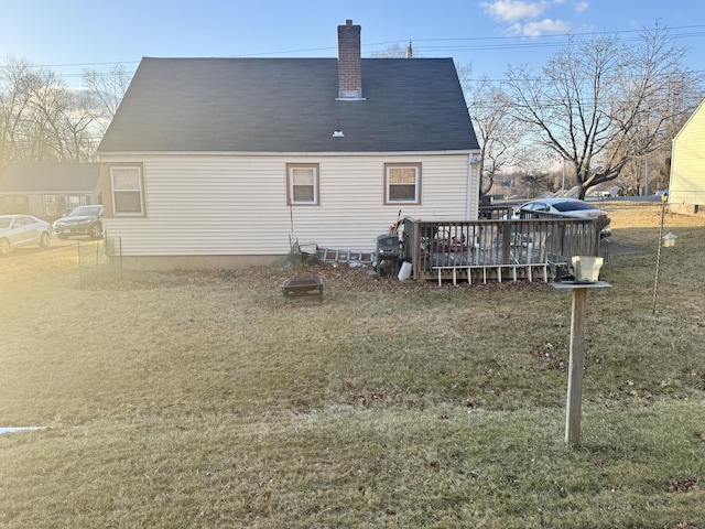 back of house featuring a deck, roof with shingles, a chimney, and a lawn