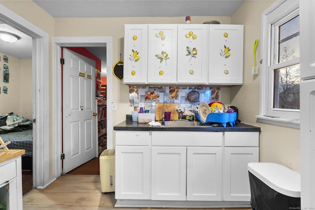 kitchen with white cabinets, a textured ceiling, light hardwood / wood-style floors, and sink