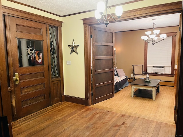 entryway with a notable chandelier, crown molding, cooling unit, wood-type flooring, and a textured ceiling