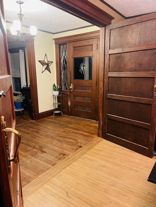 foyer entrance featuring a chandelier, hardwood / wood-style floors, a textured ceiling, and crown molding