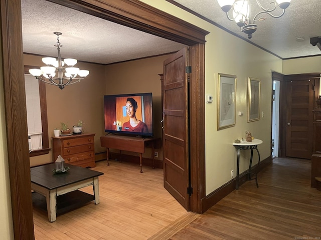 hall with crown molding, light wood-type flooring, a textured ceiling, and an inviting chandelier