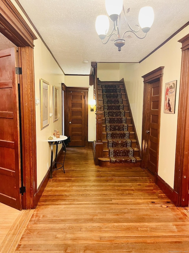 hallway with a textured ceiling, light hardwood / wood-style flooring, a notable chandelier, and crown molding