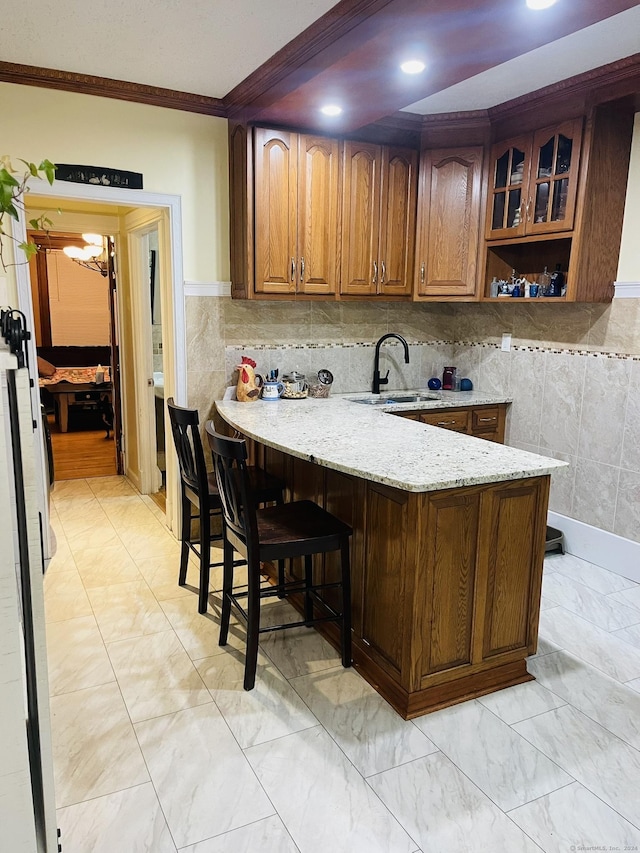 kitchen featuring sink, light stone counters, kitchen peninsula, crown molding, and a breakfast bar area