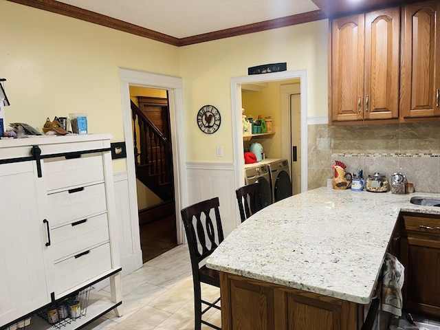 kitchen featuring backsplash, crown molding, light stone countertops, separate washer and dryer, and a breakfast bar area