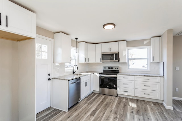 kitchen featuring tasteful backsplash, stainless steel appliances, pendant lighting, white cabinets, and light hardwood / wood-style floors