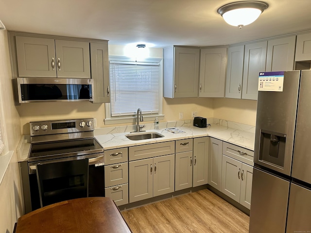 kitchen with appliances with stainless steel finishes, light hardwood / wood-style floors, gray cabinetry, and sink