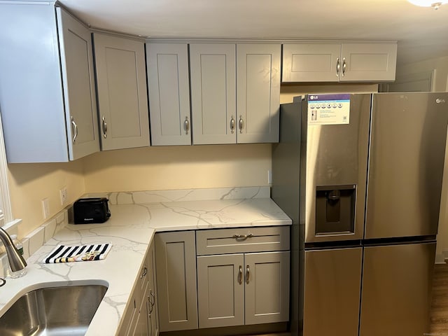 kitchen with light stone countertops, stainless steel fridge with ice dispenser, gray cabinets, and sink