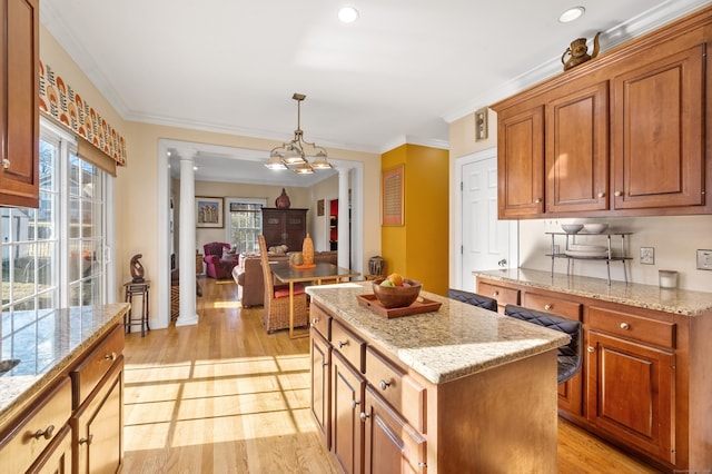 kitchen featuring pendant lighting, crown molding, light hardwood / wood-style floors, a kitchen island, and decorative columns