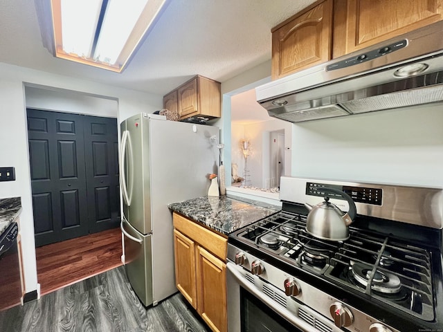 kitchen with dark stone countertops, dark hardwood / wood-style flooring, range hood, and appliances with stainless steel finishes