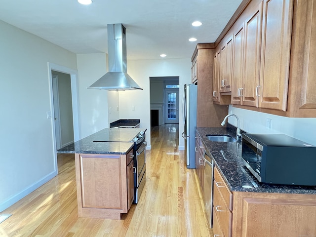 kitchen with light wood-type flooring, stainless steel appliances, sink, dark stone countertops, and range hood