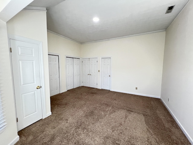 unfurnished bedroom featuring dark carpet and two closets