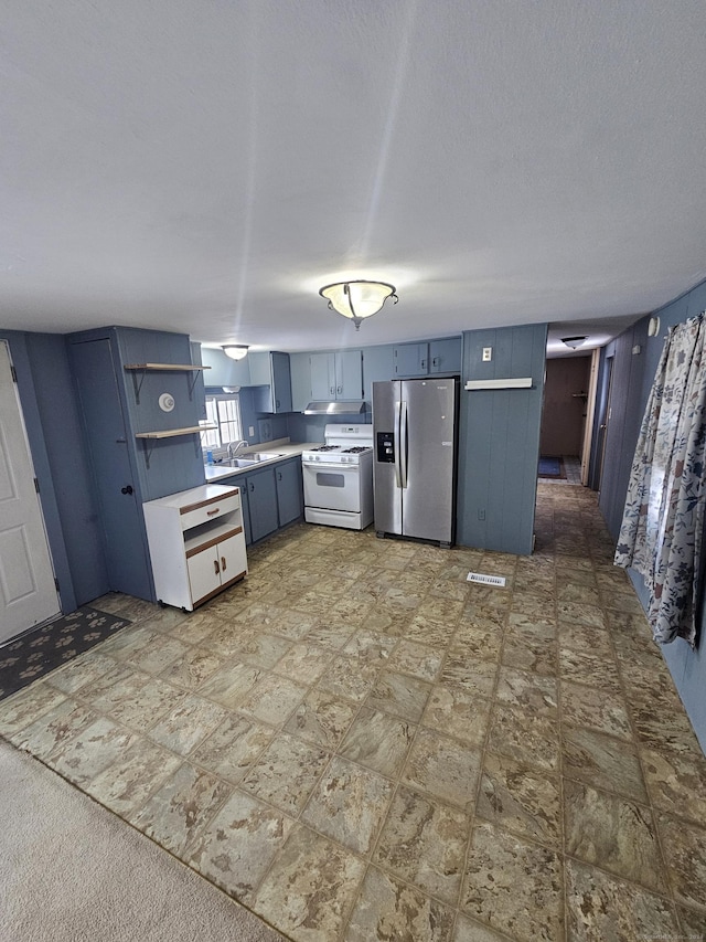 kitchen featuring sink, white range with gas stovetop, stainless steel refrigerator with ice dispenser, blue cabinets, and a textured ceiling