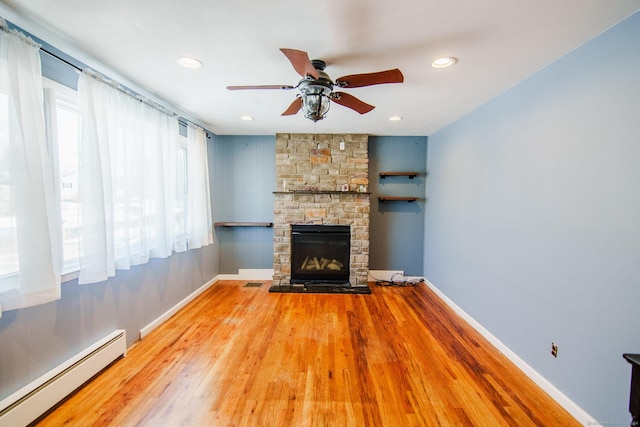 unfurnished living room with hardwood / wood-style floors, ceiling fan, a stone fireplace, and a baseboard heating unit