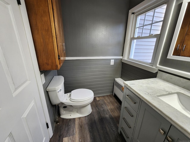 bathroom with radiator, vanity, wooden walls, hardwood / wood-style floors, and toilet