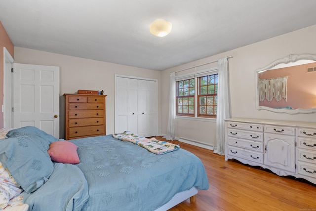 bedroom with light wood-type flooring, baseboard heating, and a closet