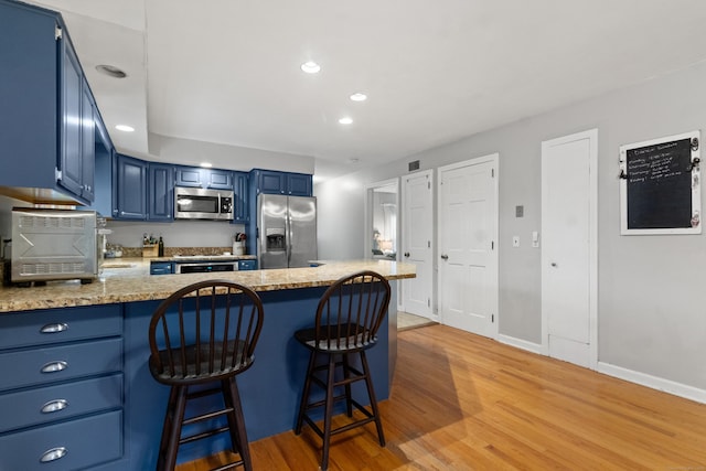 kitchen featuring kitchen peninsula, stainless steel appliances, blue cabinets, light hardwood / wood-style floors, and a breakfast bar area