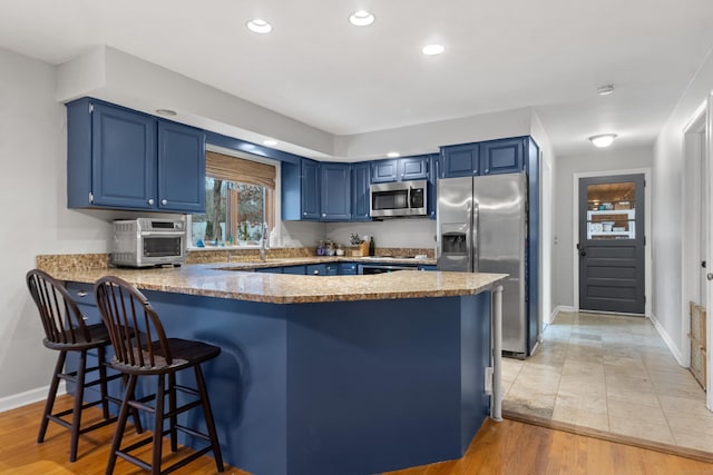 kitchen featuring blue cabinetry, kitchen peninsula, stainless steel appliances, and light hardwood / wood-style flooring