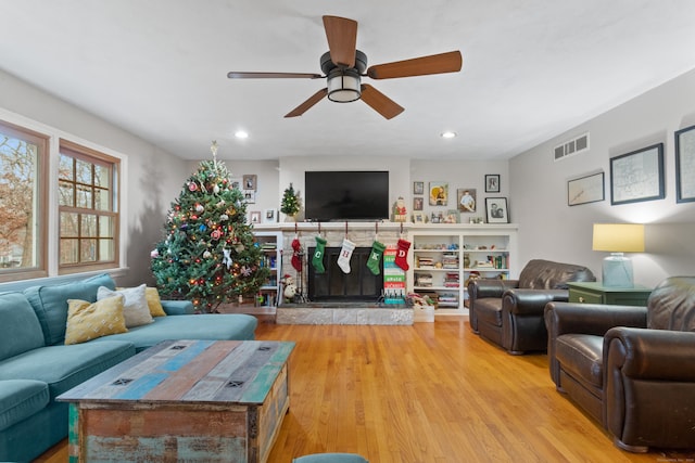 living room with light hardwood / wood-style flooring, ceiling fan, and a stone fireplace