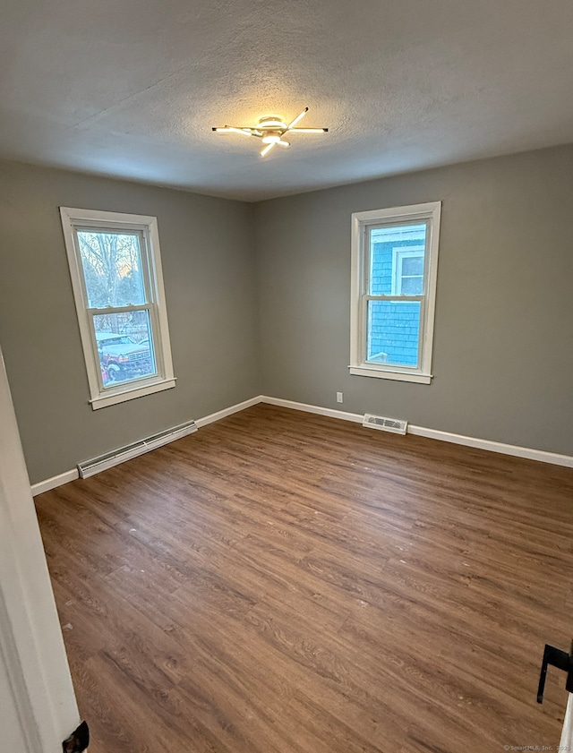 unfurnished room with dark wood-type flooring, a baseboard radiator, and a textured ceiling