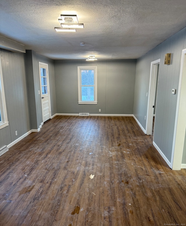 spare room featuring dark hardwood / wood-style flooring, wooden walls, and a textured ceiling