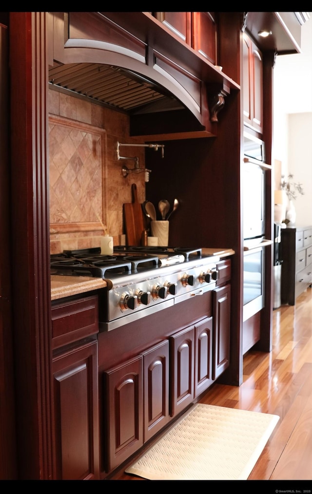 kitchen featuring tasteful backsplash, stainless steel appliances, ventilation hood, and light wood-type flooring