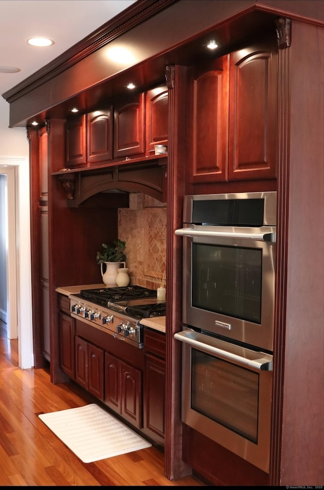 1461 Bunker Hill Rd, Watertown, CT 06795 - kitchen with reddish brown cabinets, light wood-style flooring, decorative backsplash, appliances with stainless steel finishes, and light countertops