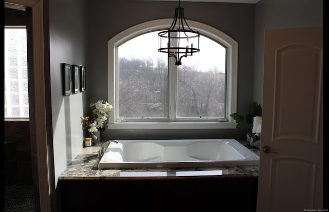 bathroom featuring a notable chandelier, a bathtub, and a wealth of natural light