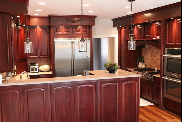 kitchen with tasteful backsplash, hanging light fixtures, kitchen peninsula, stainless steel appliances, and light wood-type flooring