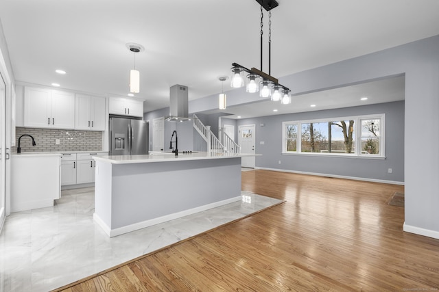 kitchen with white cabinets, stainless steel fridge, decorative light fixtures, and a center island with sink